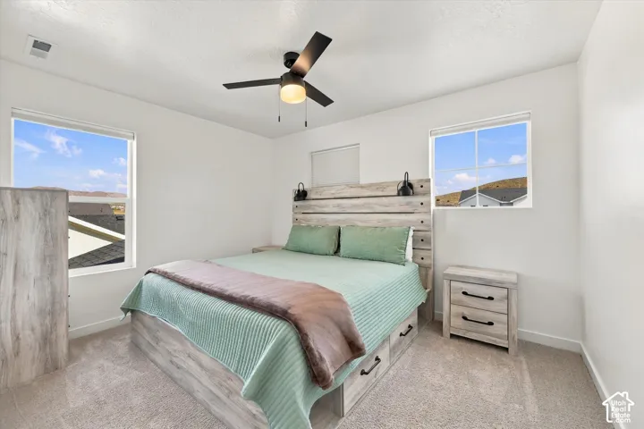 White walls featuring two windows, a ceiling fan with light, and light-colored carpet flooring