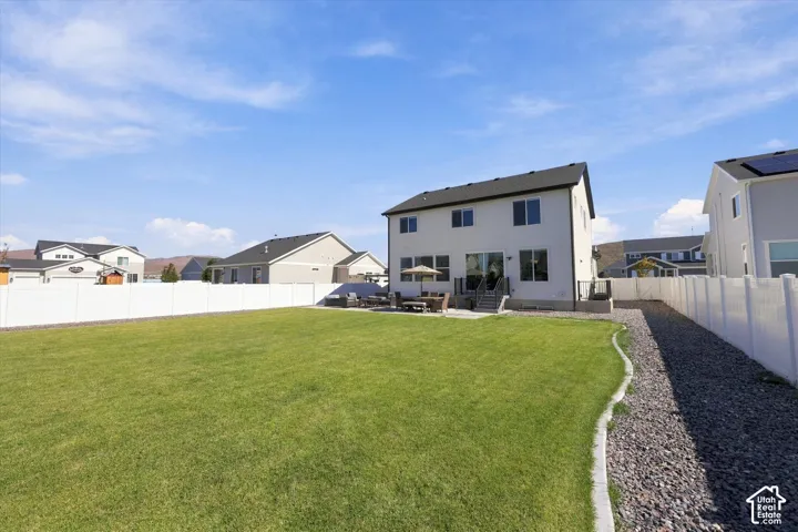 Expansive green lawn, white privacy fencing, rear patio, sliding glass door access, and a gravel pathway