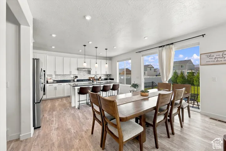 Open-concept living area with wood-finish flooring, white cabinetry, dark countertops, and a full-height tile backsplash