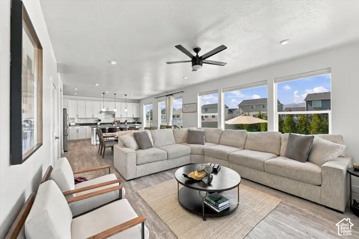 Open-concept living area featuring wood-finish flooring, a contemporary ceiling fan, and multiple large windows