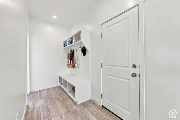 Entryway featuring wood-finish flooring, white paneled door, and built-in storage bench with upper shelving and coat hooks