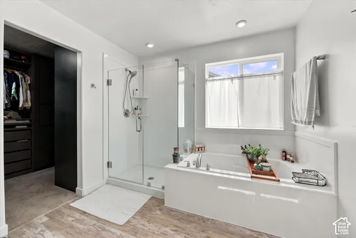 Built-in soaking tub, glass-enclosed shower, wood-finish flooring, recessed lighting, and built-in closet storage