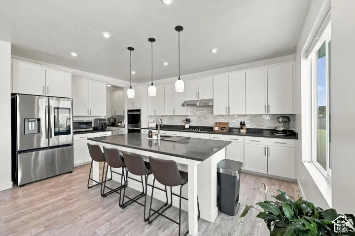 Kitchen featuring white cabinetry, stainless steel appliances, dark countertops, a large island with pendant lighting, and wood-finish flooring