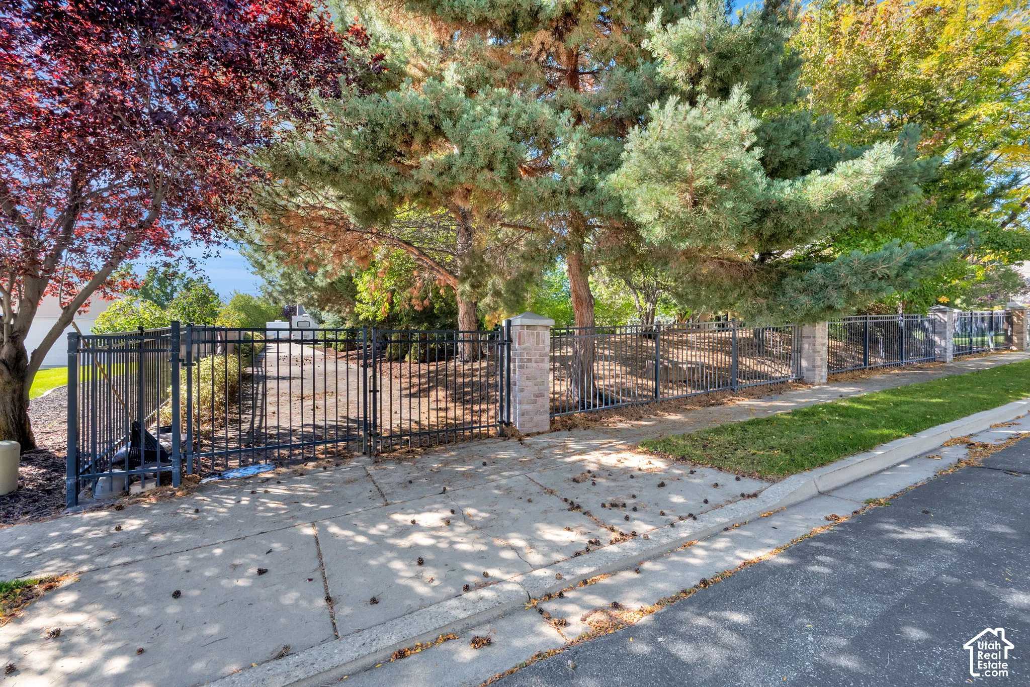 Wrought iron fencing with brick columns, mature trees, and a concrete sidewalk