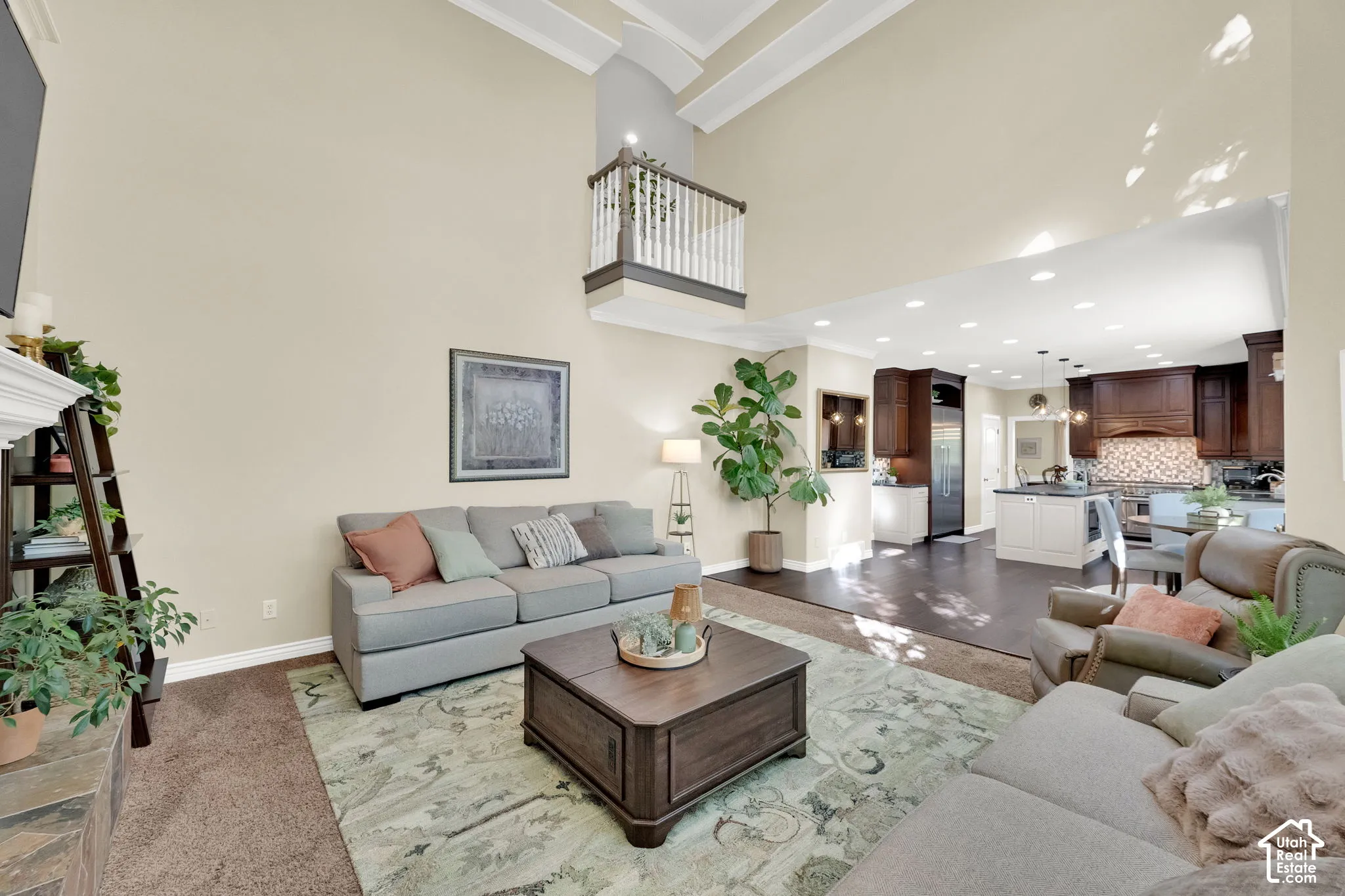 Soaring vaulted ceilings with architectural beams, open-concept design, kitchen with dark wood cabinetry and contrasting island, recessed lighting, and a stone-clad fireplace
