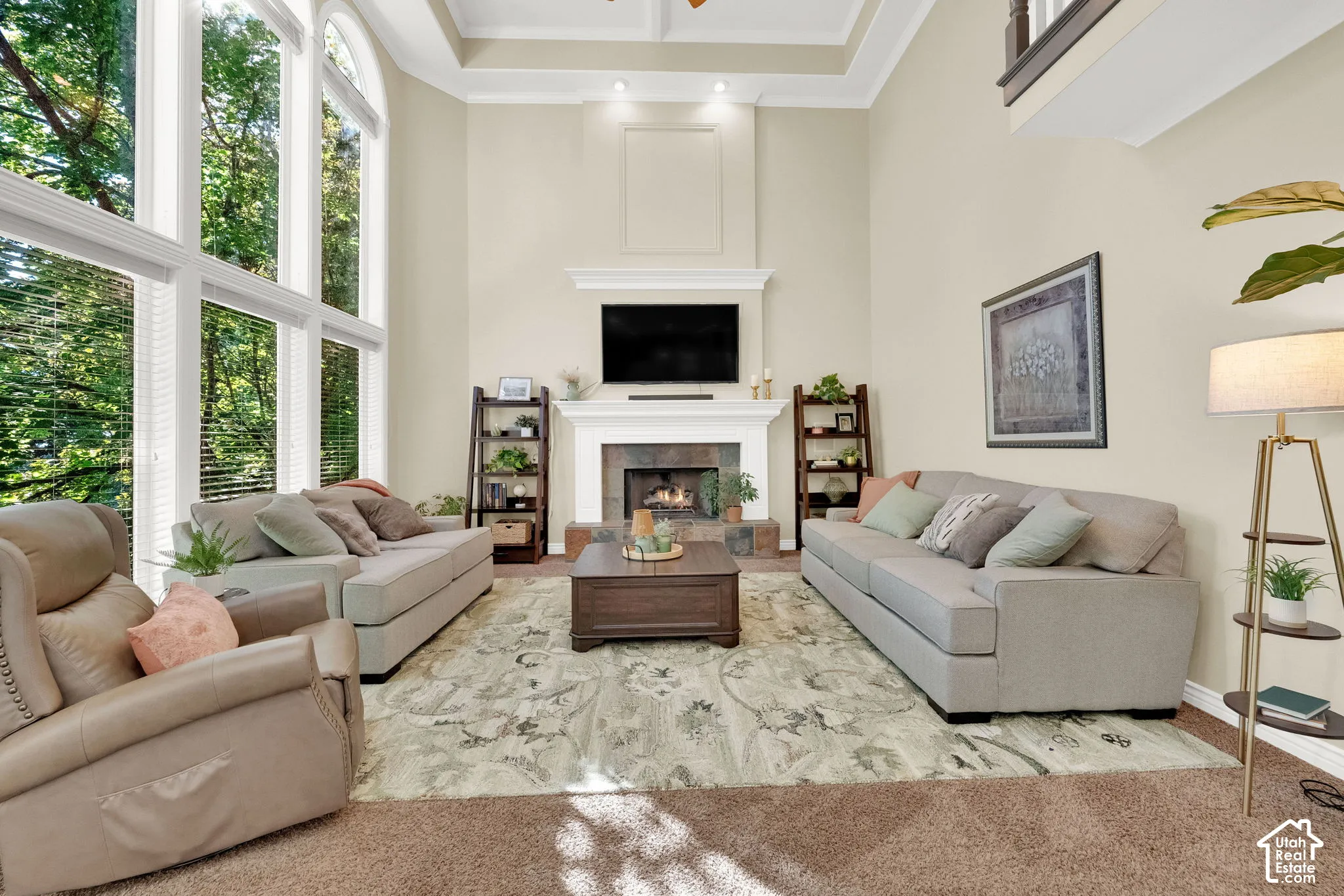 Two-story windows, vaulted ceiling with crown molding, tray ceiling detail, fireplace with stone surround, and a mantel