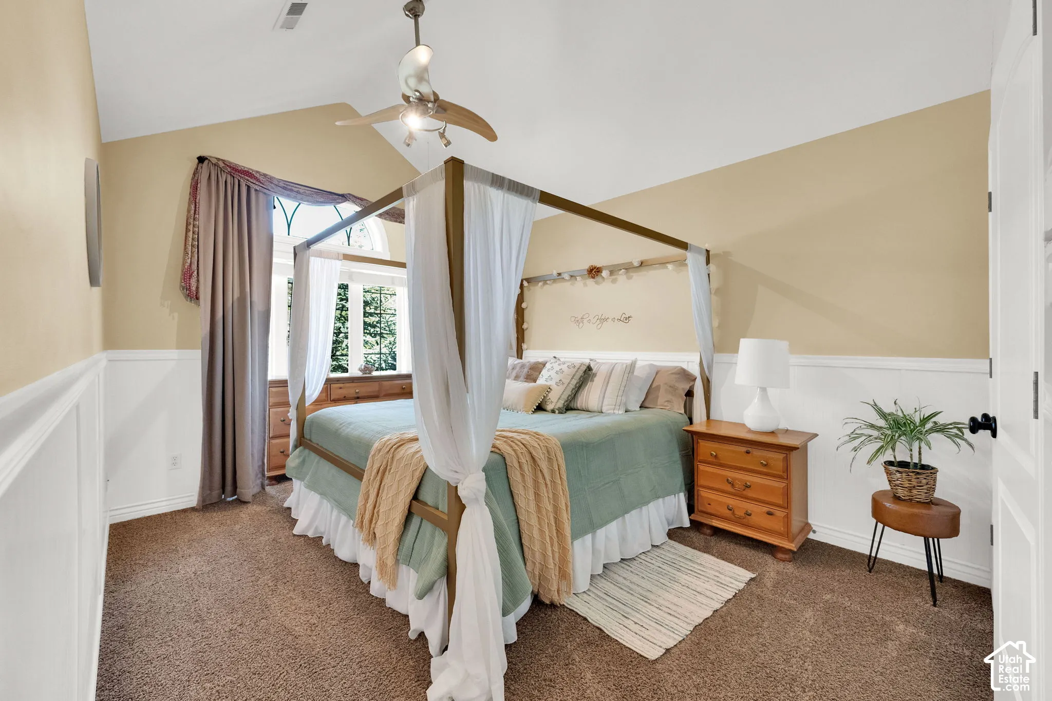 Vaulted ceiling with an attached ceiling fan, large window with arched transom, and wainscoting
