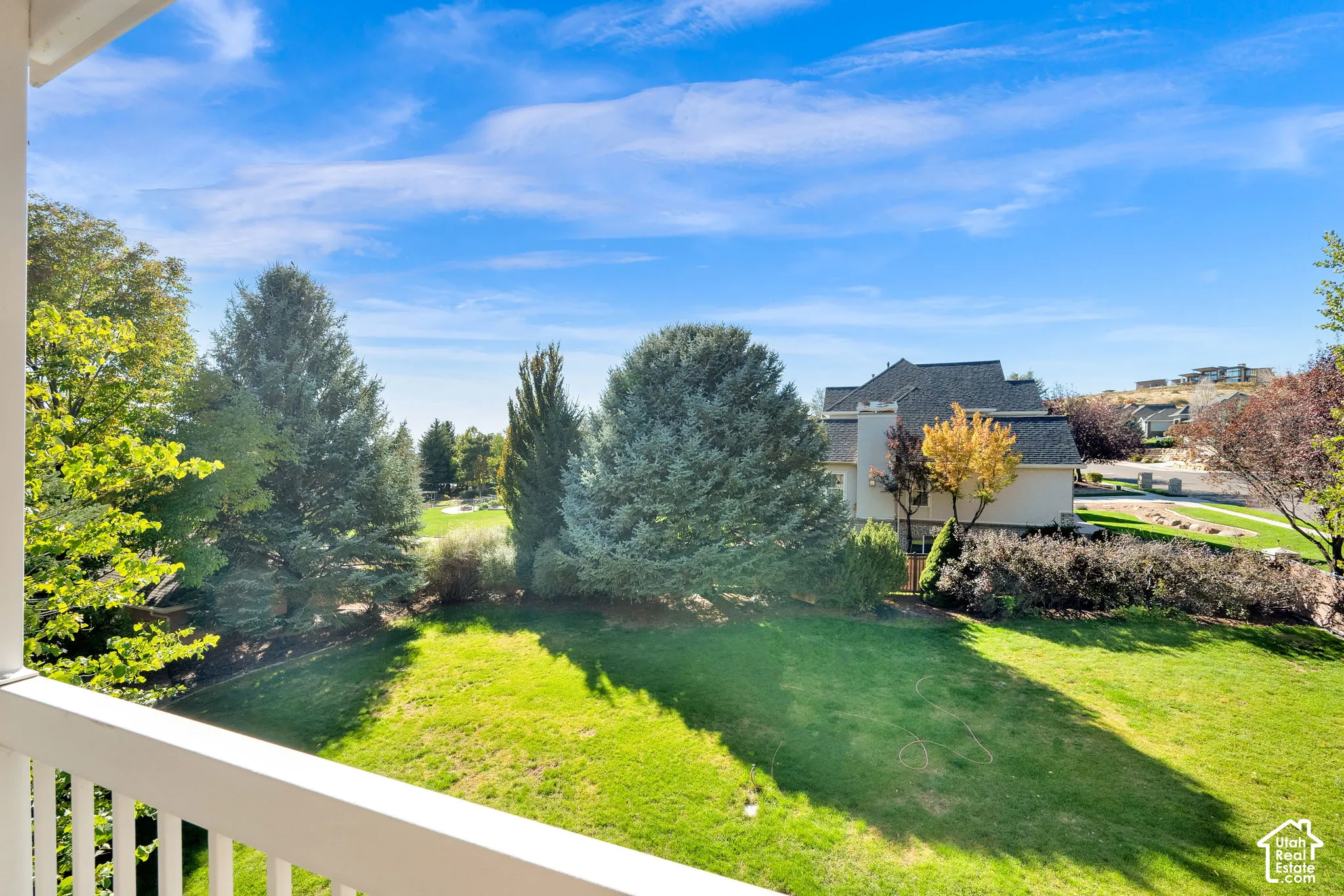 Expansive green lawn surrounded by mature trees, featuring a distant golf course and a paved pathway