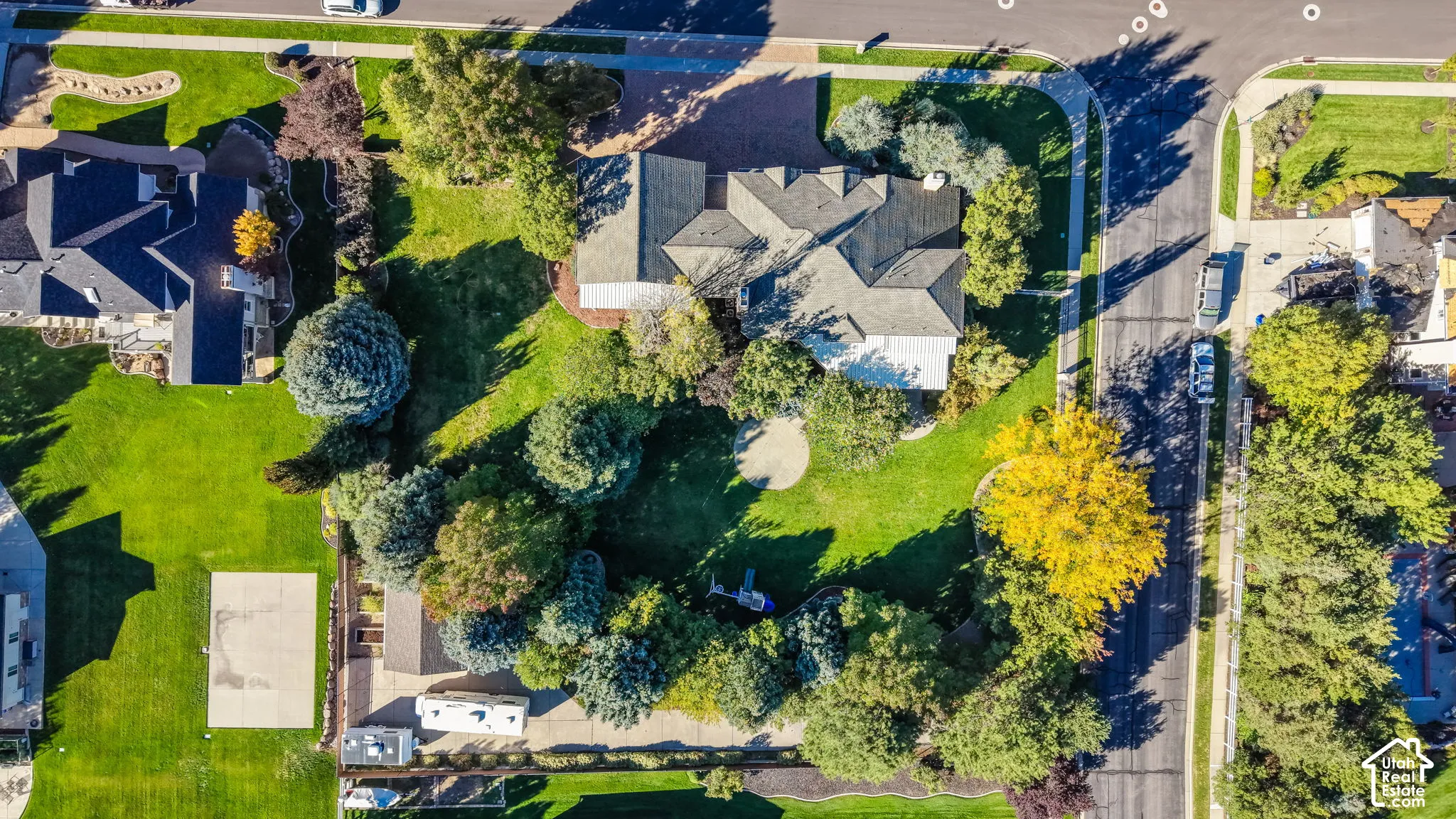 Expansive property with a gabled roofline, mature trees, manicured lawns, and a concrete sport court