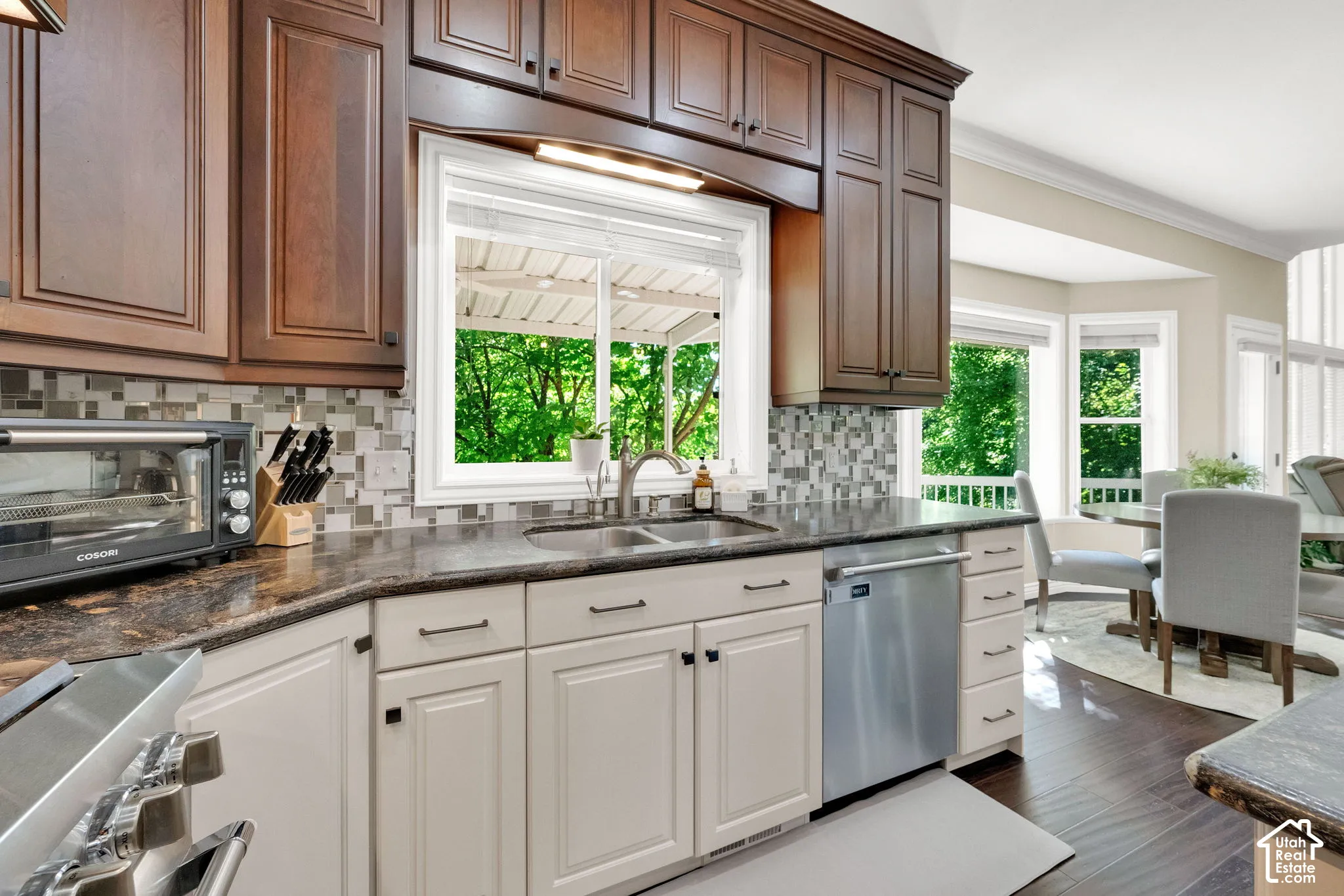 Two-tone cabinetry with dark wood-finish upper cabinets and light lower cabinets, dark stone-finish countertops, mosaic tile backsplash, stainless steel dishwasher, and a double basin sink with a gooseneck faucet