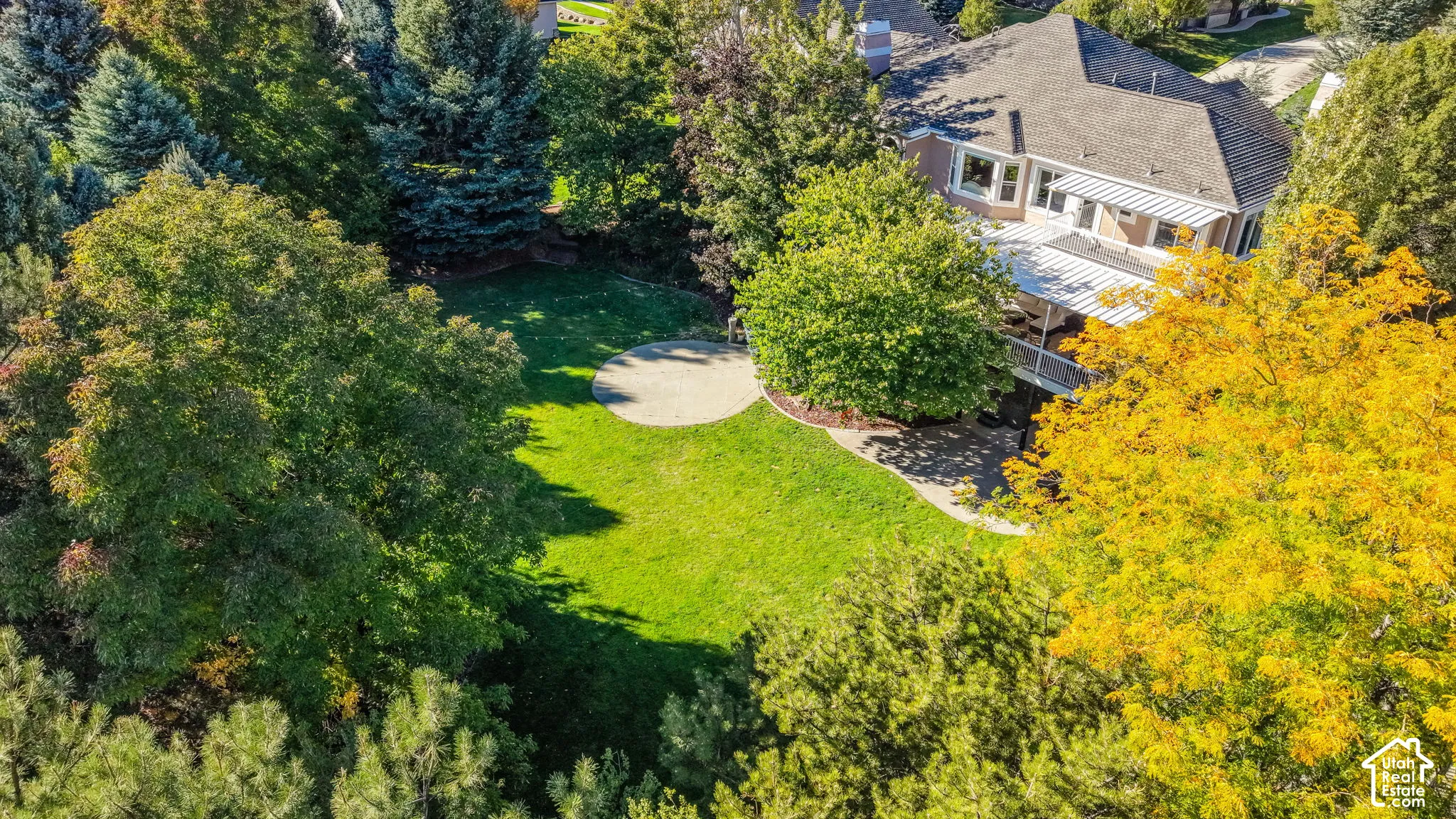 Expansive green lawn with a circular paved patio, mature trees, and a multi-level deck with a covered area