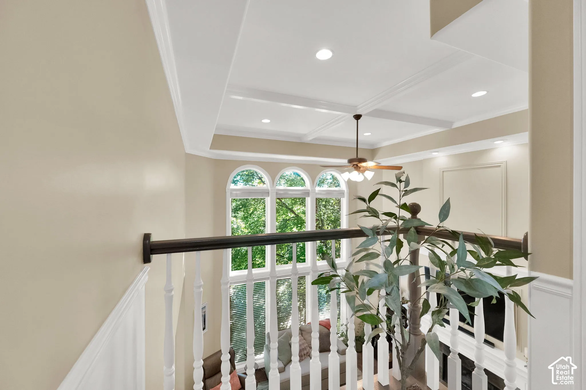Wainscoting and crown molding details, coffered ceiling with recessed lighting, arched windows, and a ceiling fan