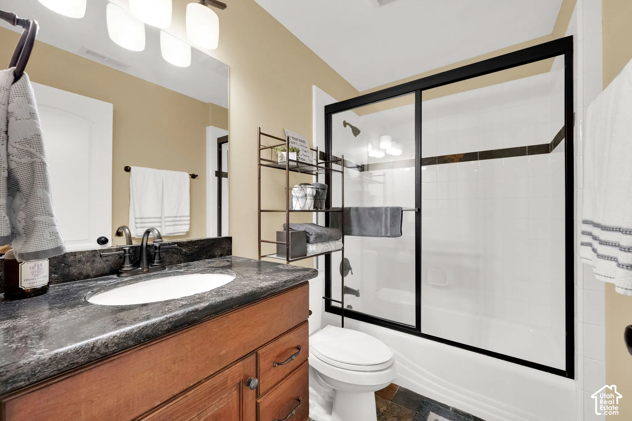 Wood-finish vanity with an undermount sink, dark countertop, oil-rubbed bronze faucet, and a shower-tub combination with sliding glass doors