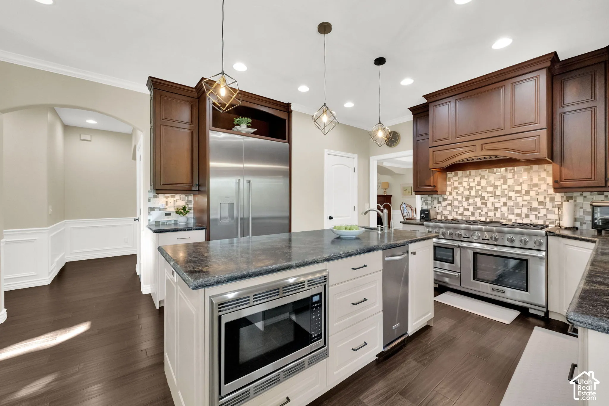 Gourmet kitchen featuring stainless steel appliances, dark wood cabinetry, a large kitchen island with built-in microwave, and pendant lighting