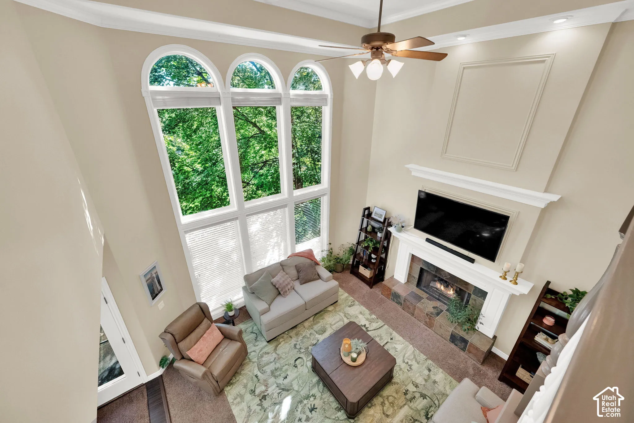 Vaulted living area featuring a central fireplace with a stone hearth, a multi-pane window wall, a ceiling fan, and recessed lighting