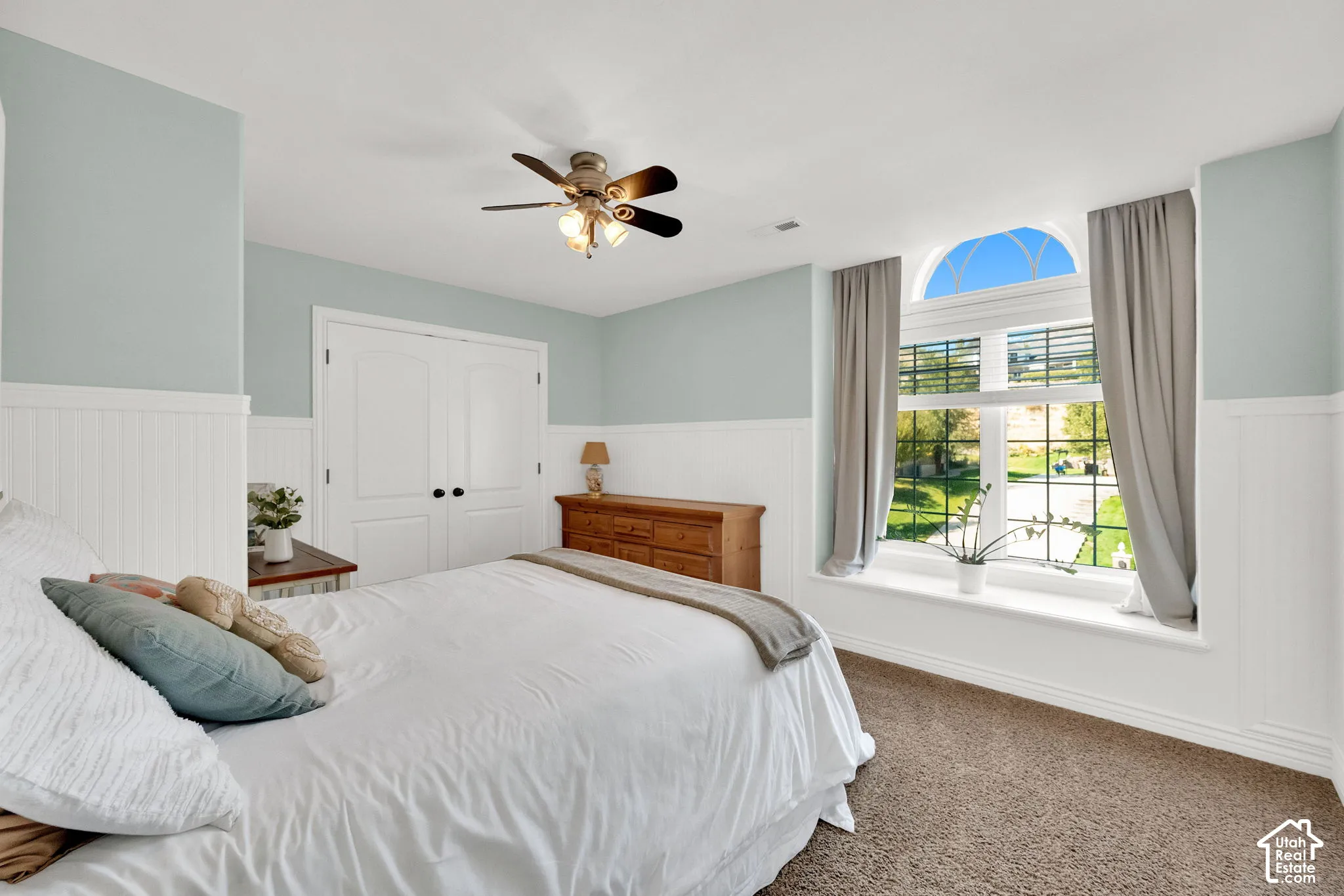 Arch-top window with exterior landscape, ceiling fan, carpet flooring, and paneled wainscoting