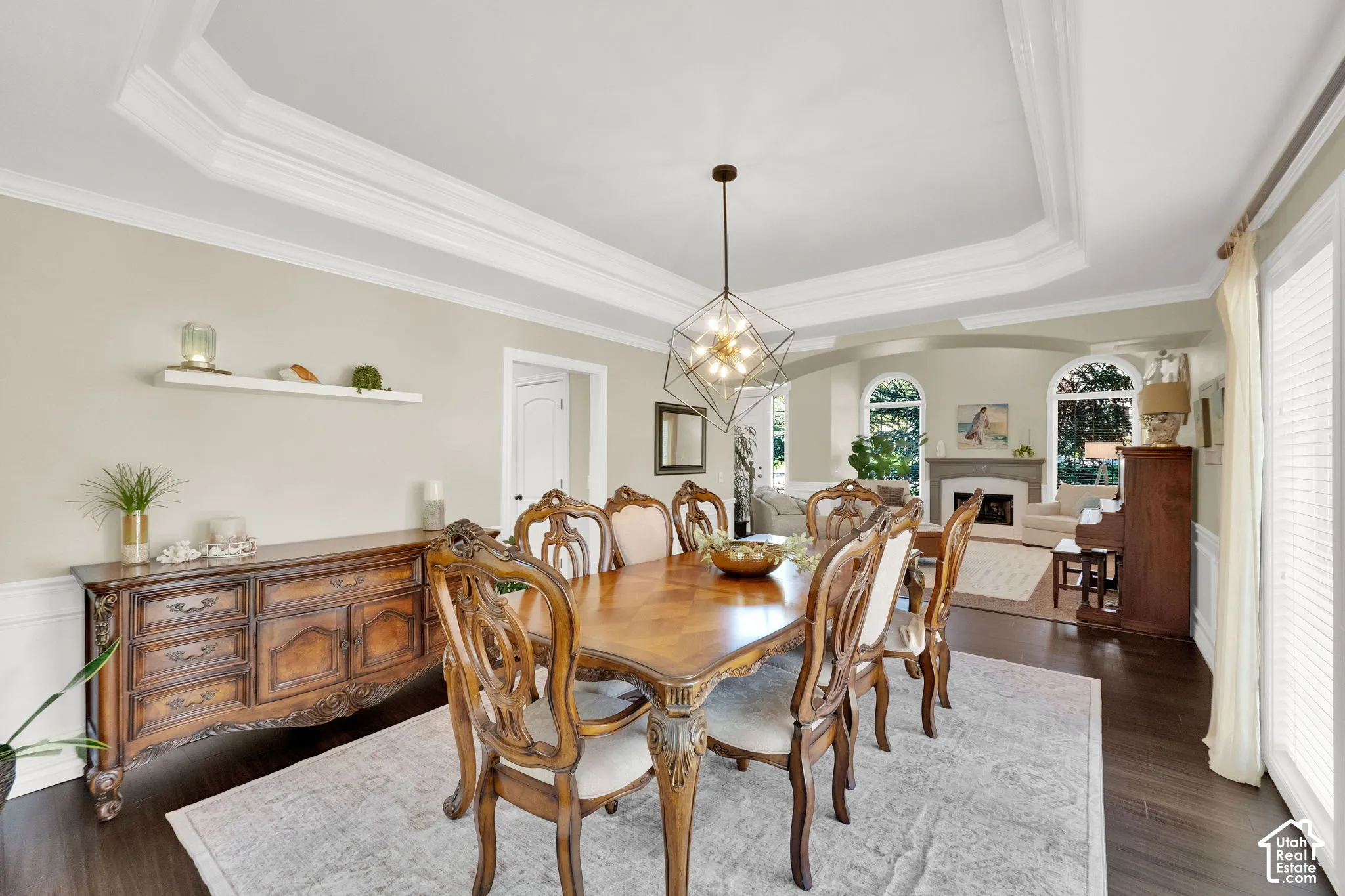 Tray ceiling with crown molding, dark wood-finish flooring, white wainscoting, and an open doorway