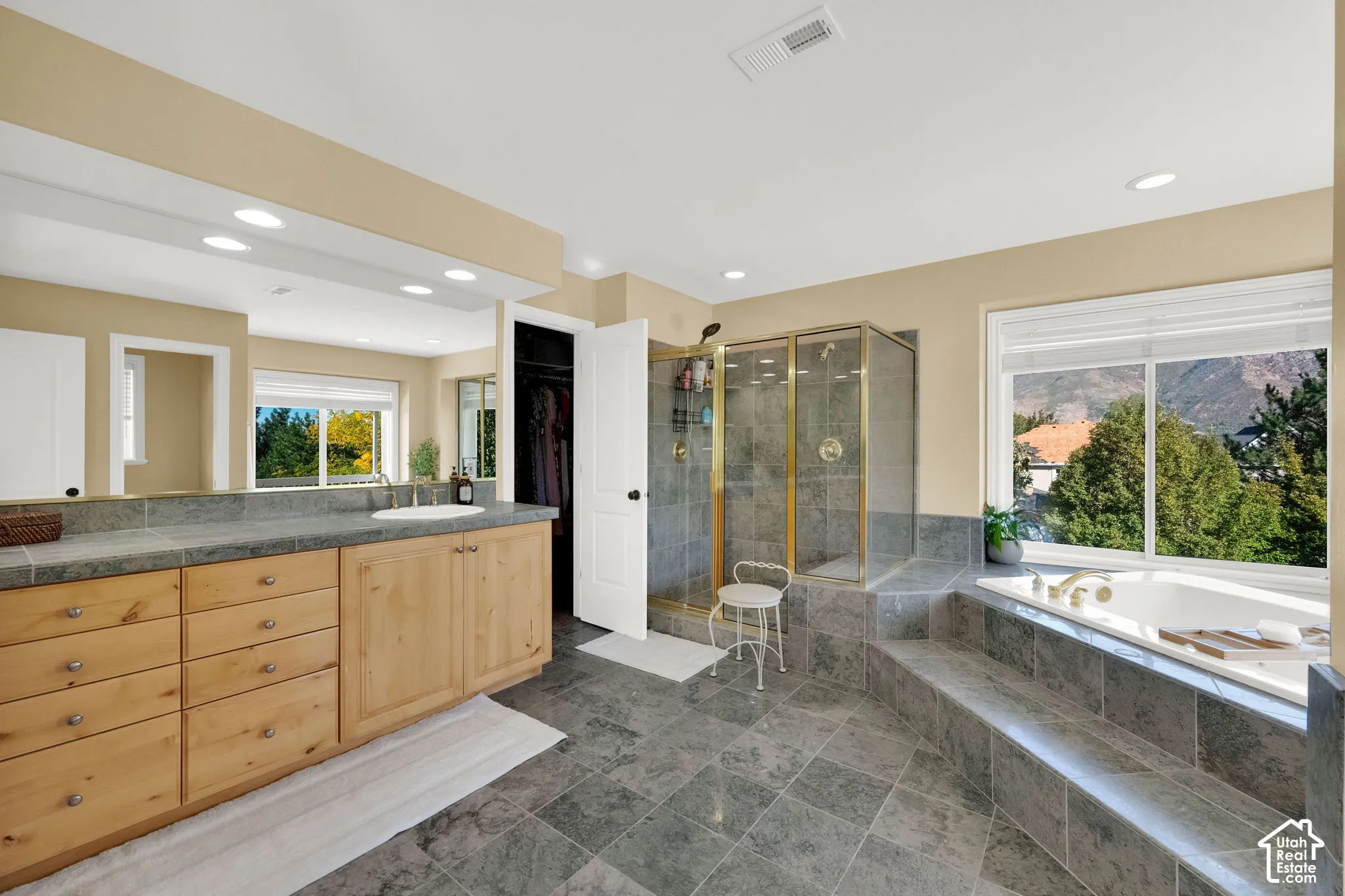Spacious bathroom featuring natural wood vanity cabinetry, stone countertop, integrated soaking tub, and a glass-enclosed shower
