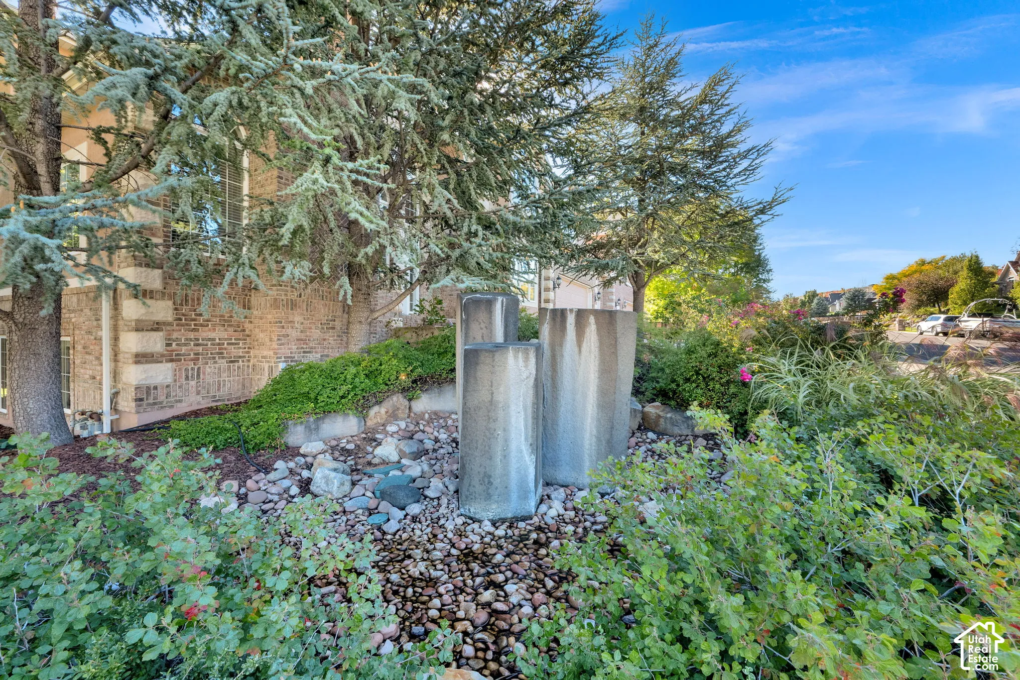 Brick exterior with stone accents, mature trees, and a decorative water feature with river rock