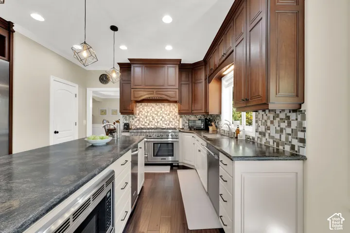 Kitchen featuring wood-finish flooring, dark stone countertops, wood cabinetry, stainless steel appliances, and a mosaic tile backsplash