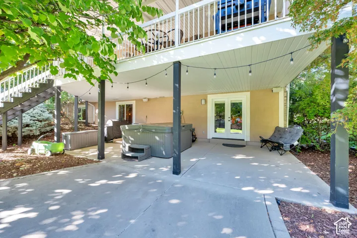 Lower-level concrete patio with string lighting, direct exterior access via French doors, and mature landscaping