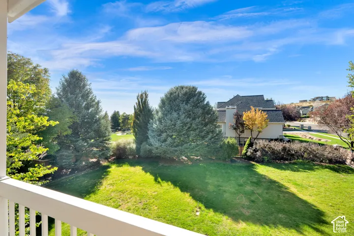 Expansive green lawn surrounded by mature trees, featuring a distant golf course and a paved pathway