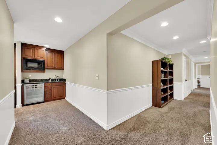 Wet bar with wood cabinetry, microwave, undermount sink, beverage refrigerator, and granite-style countertop