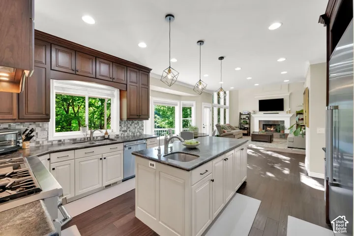 Kitchen featuring wood-finish flooring, two-tone cabinetry, a central island with a sink, stainless steel appliances, and recessed lighting