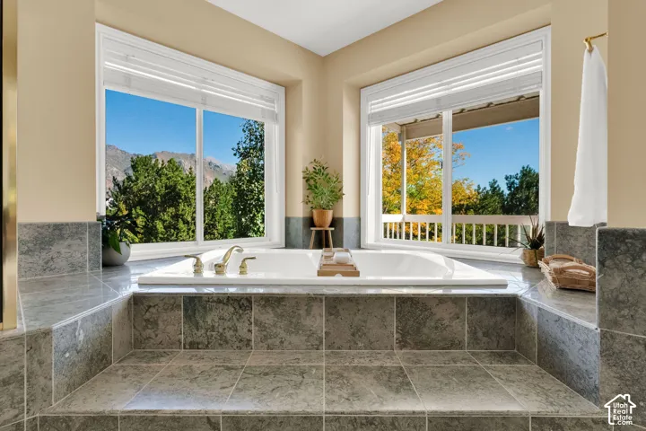Built-in soaking tub with deck-mounted fixtures, surrounded by grey tile flooring and wall accents