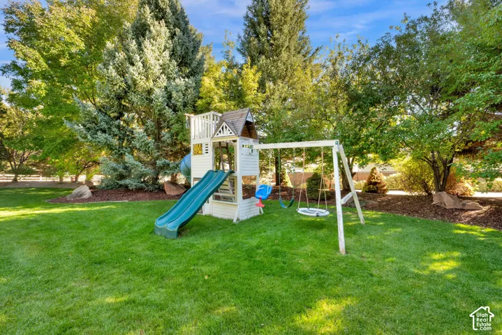 Expansive green lawn with mature trees and a play structure featuring a slide and swing set