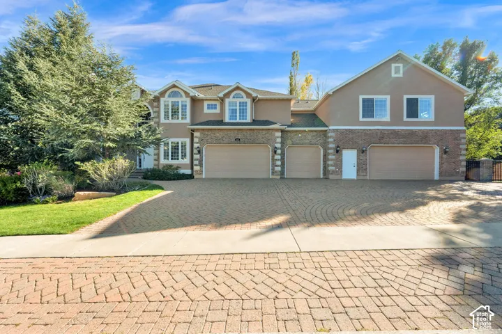 Stucco and brick exterior with multiple arched windows, prominent bay window, and a spacious paver driveway leading to three garage doors