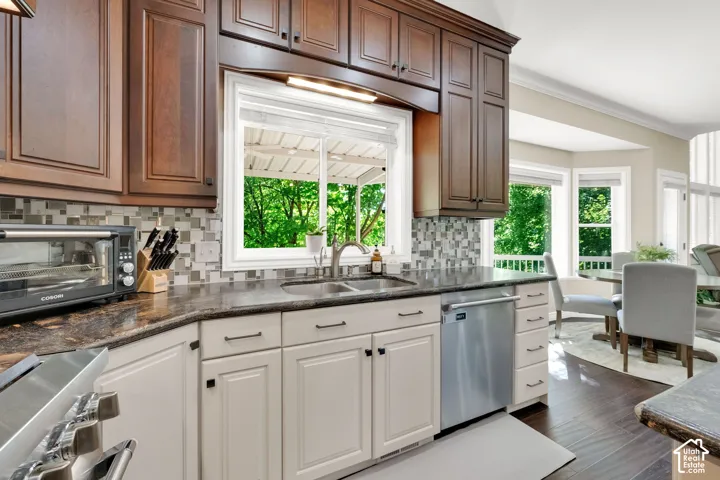 Two-tone cabinetry with dark wood-finish upper cabinets and light lower cabinets, dark stone-finish countertops, mosaic tile backsplash, stainless steel dishwasher, and a double basin sink with a gooseneck faucet