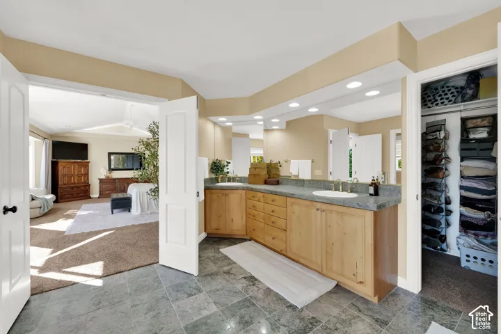 Dual sinks with wood-finish cabinetry, recessed lighting, and a walk-in closet with built-in shelving