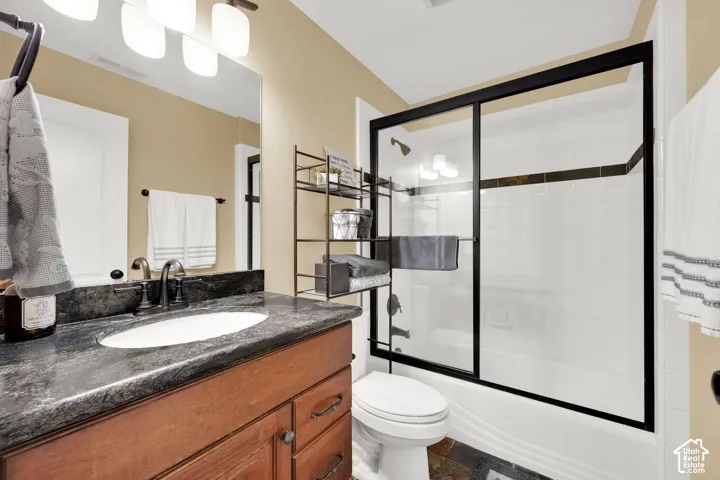 Wood-finish vanity with an undermount sink, dark countertop, oil-rubbed bronze faucet, and a shower-tub combination with sliding glass doors