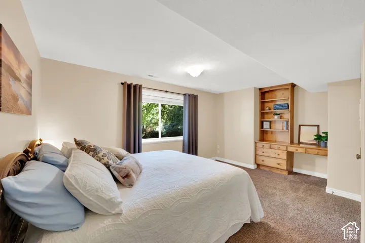 Recessed window with exterior foliage, built-in wooden shelving, integrated wooden desk, and neutral carpet flooring