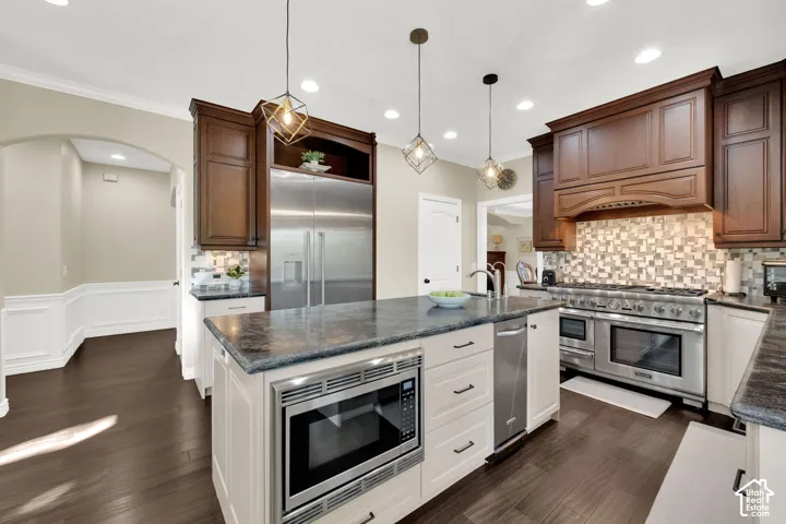 Gourmet kitchen featuring stainless steel appliances, dark wood cabinetry, a large kitchen island with built-in microwave, and pendant lighting