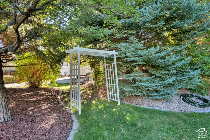 White pergola, mature trees, manicured lawn, bark ground cover, gravel landscaping