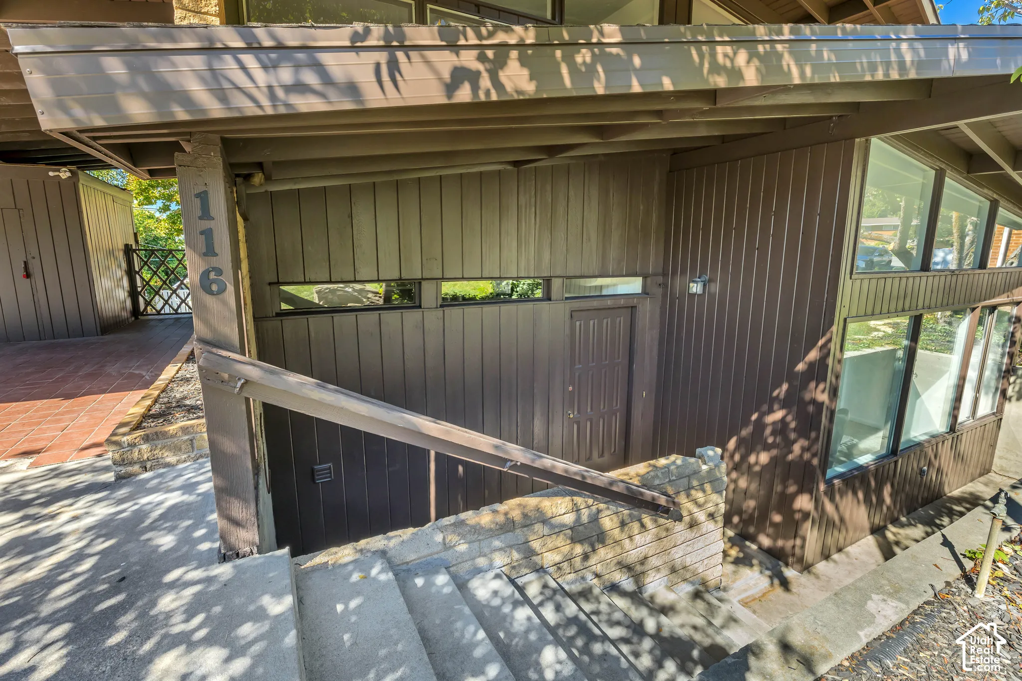 Contemporary exterior featuring brown vertical siding, integrated windows, a covered entryway, and concrete stairs with a wood-finish railing