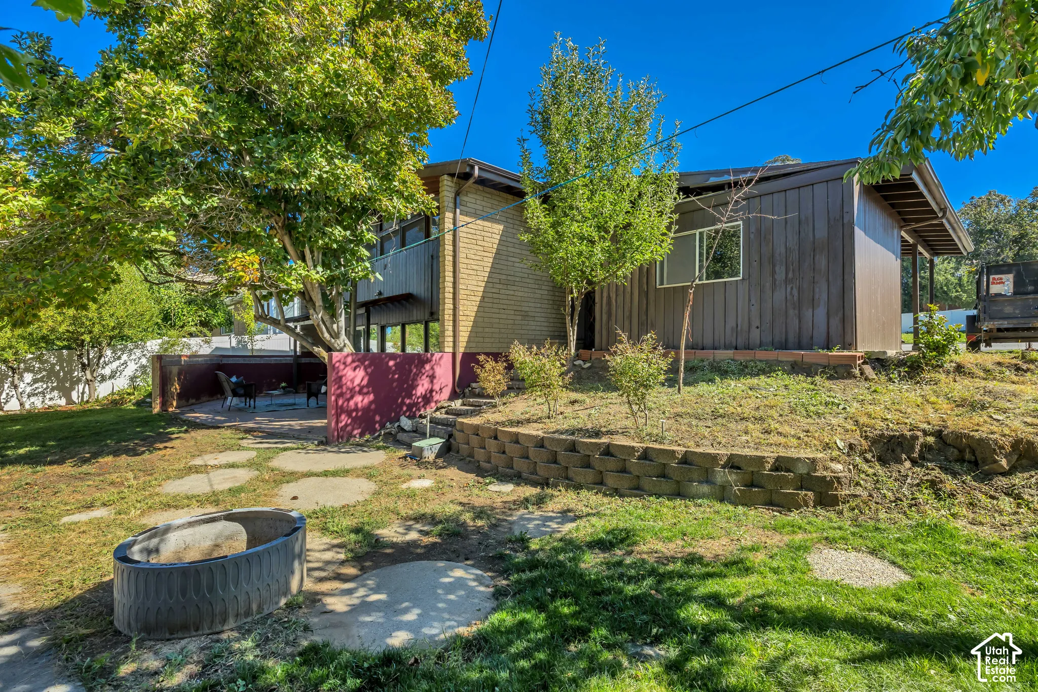 Rear exterior featuring concrete paver patio, brick retaining wall, and mature trees