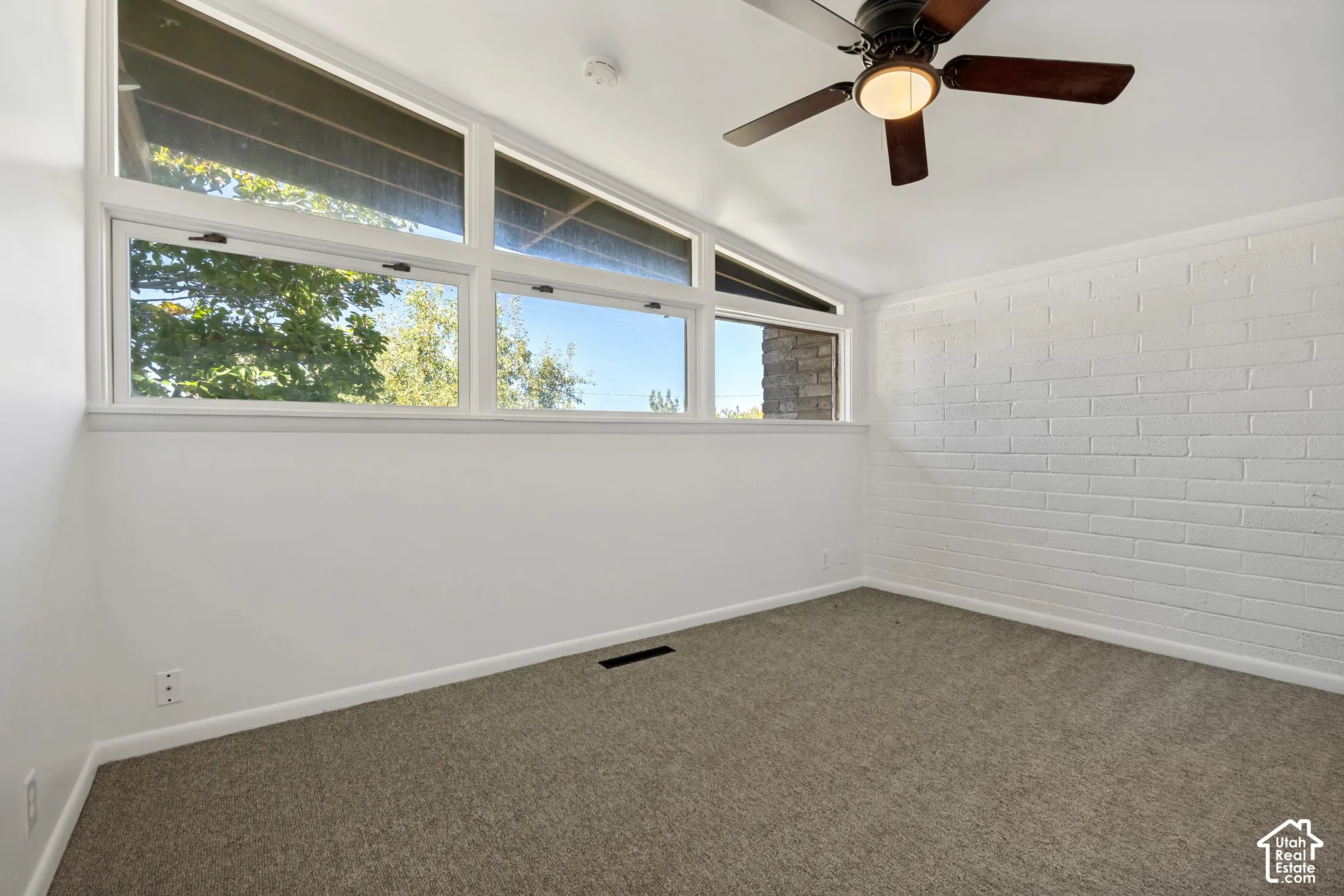 Angled ceiling with a dark wood-finish ceiling fan, white painted brick accent wall, and large upper transom windows