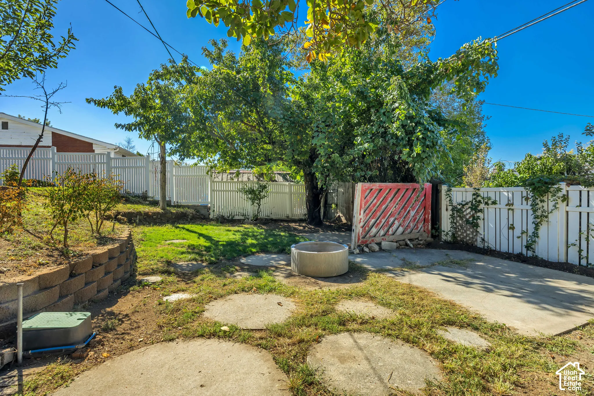 Expansive backyard featuring a concrete patio, stepping stones, concrete retaining wall, and white privacy fencing