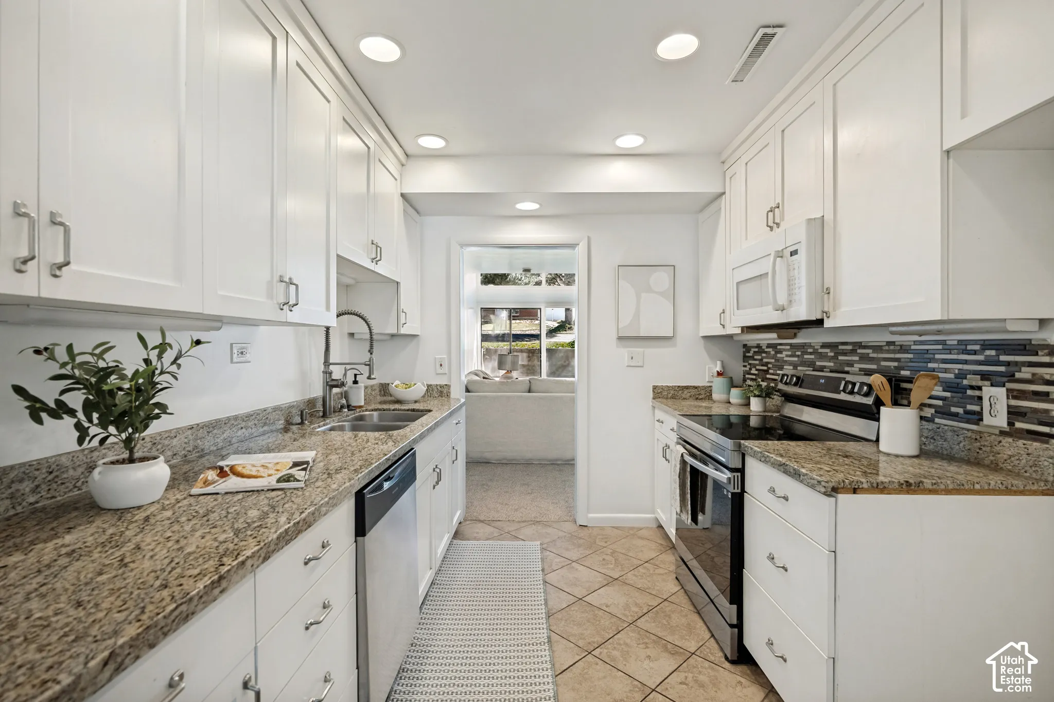 White cabinetry, granite countertops, tile flooring, stainless steel appliances, and a mosaic tile backsplash