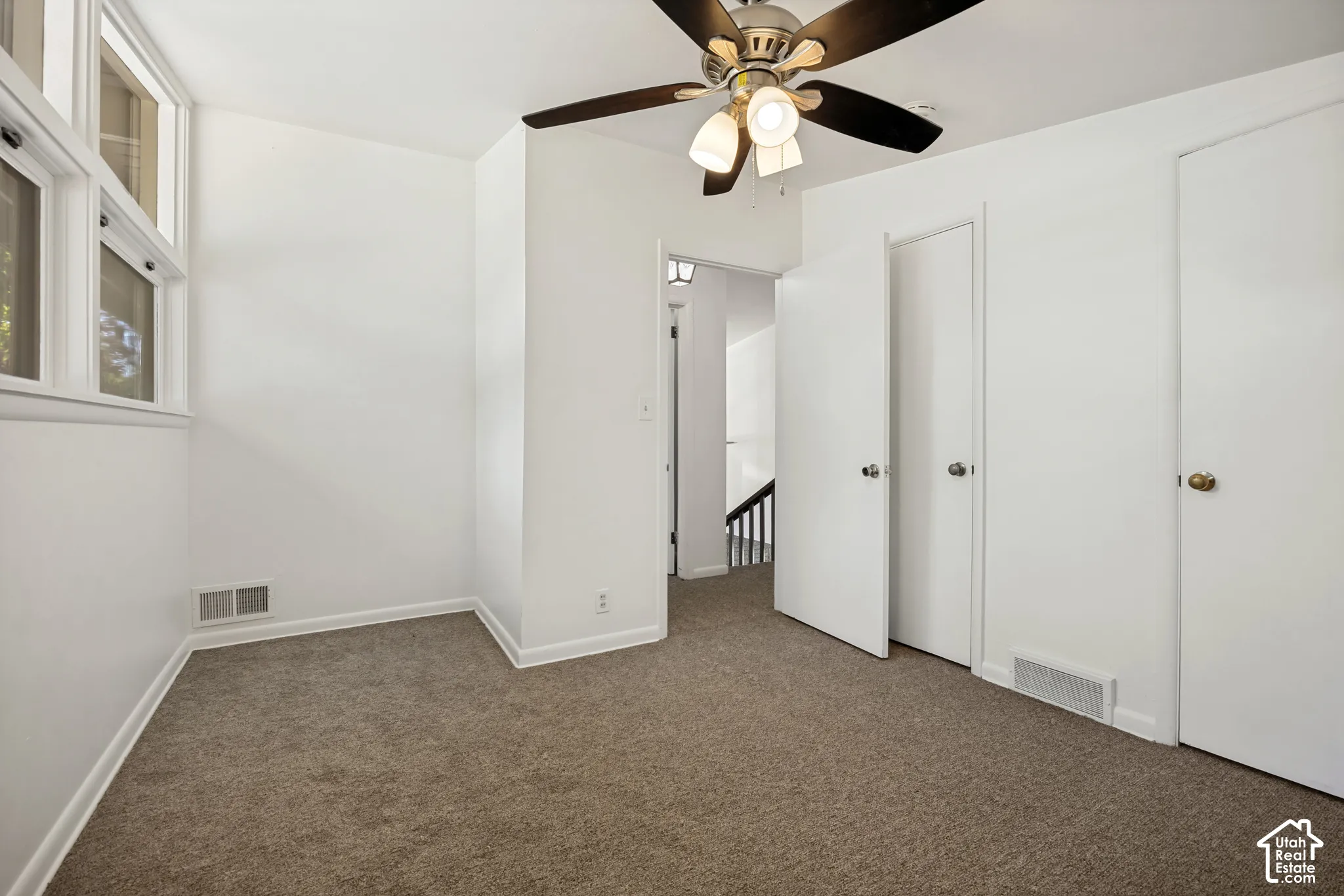 Brown carpet flooring, white painted walls, white trim, ceiling fan light fixture, and multiple white doors