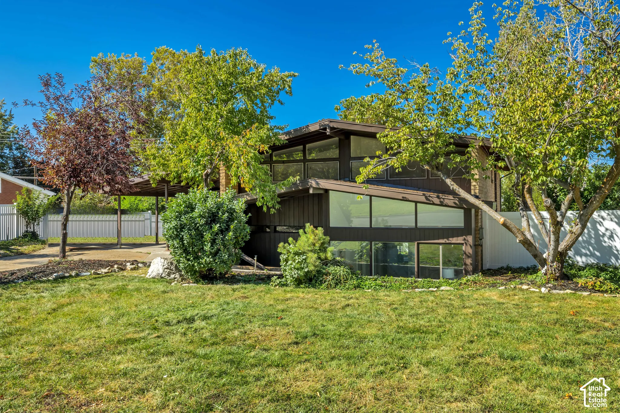 Multi-level exterior with extensive glazing, covered carport, and established landscaping