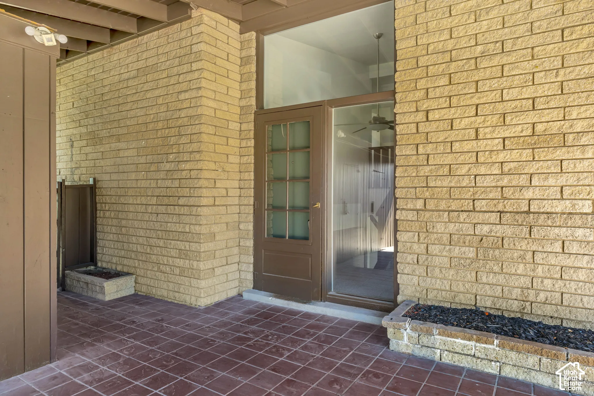 Brick exterior featuring a wood-frame door with glass panels, an expansive fixed glass panel, and a tiled patio