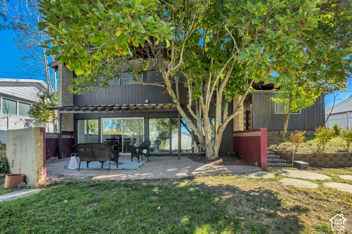 Expansive rear patio featuring a pergola, sliding glass doors, concrete paver accents, and a tiered retaining wall