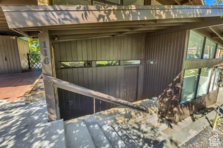Contemporary exterior featuring brown vertical siding, integrated windows, a covered entryway, and concrete stairs with a wood-finish railing