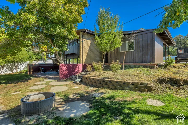 Rear exterior featuring concrete paver patio, brick retaining wall, and mature trees