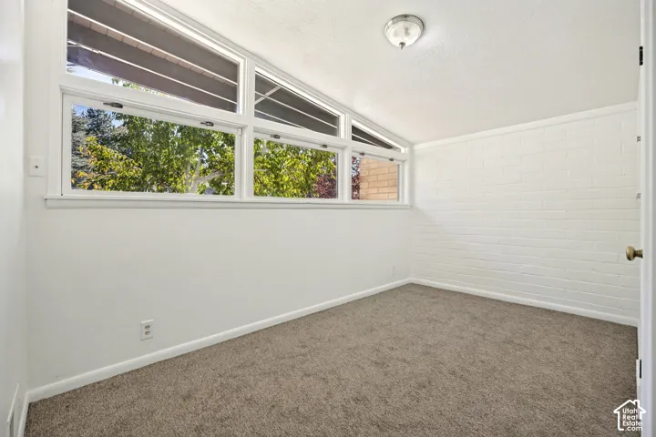 Expansive window arrangement with transom windows, white brick accent wall, flush-mount ceiling light, and neutral-toned carpeting