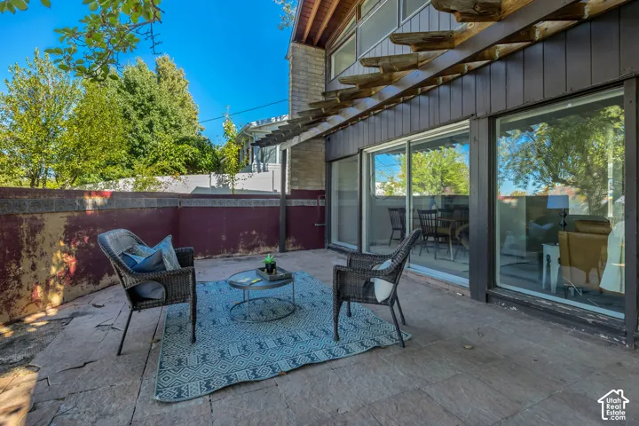Stone patio with a wood pergola, featuring sliding glass doors and a privacy wall